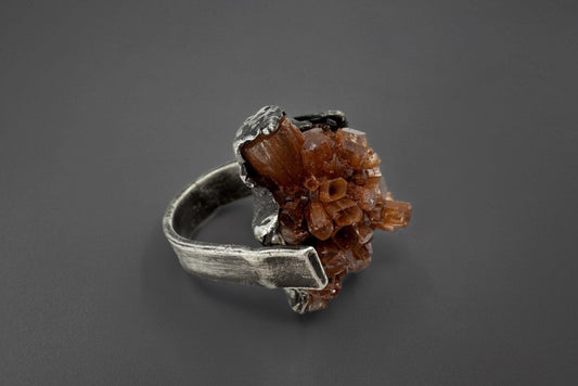 Silver ring with a brown aragonite crystal on a dark gray background