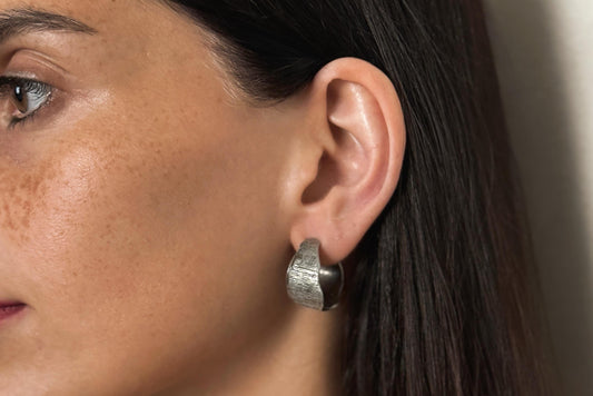 Close-up of a woman's ear wearing a silver hoop earring with a neutral background