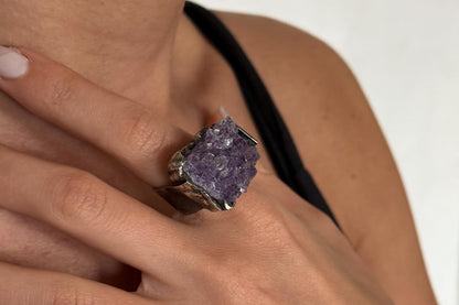 Close-up of a hand wearing a ring with a purple amethyst gemstone on a white background